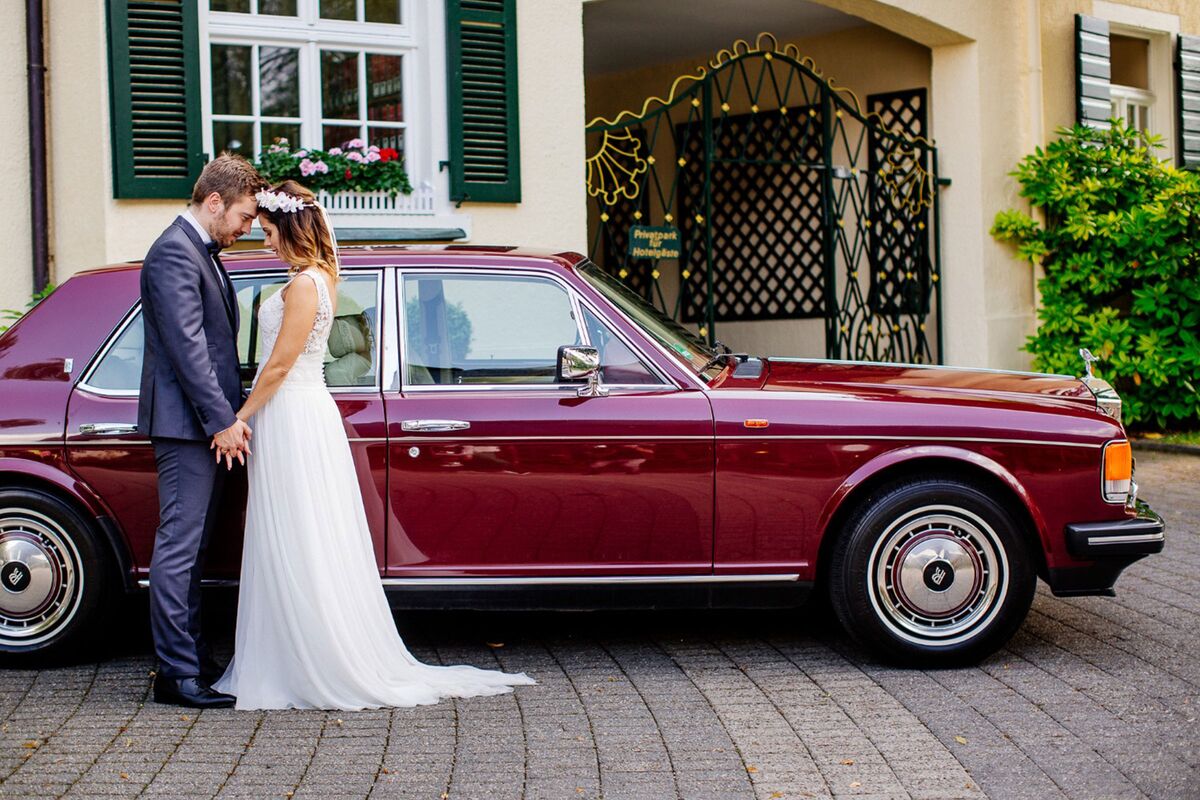 Red vintage Rolls Royce of the hotel with bridal couple in front of it